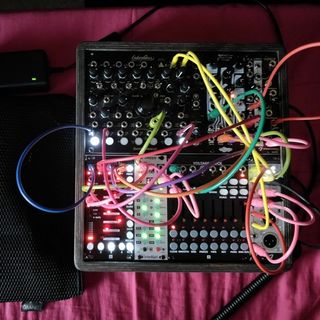 A 48hp eurorack case on red bed sheets with colorful cables